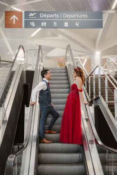 Dans un aéroport, le marié et la mariée en robe rouge se font face sur deux escalators voisins