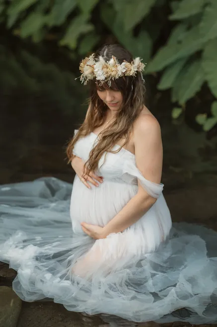 Future maman assise dans l’eau, robe de tulle déployée autour d’elle et couronne de fleurs