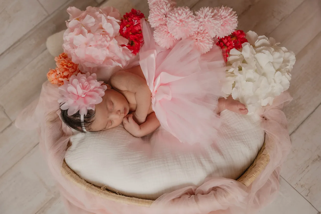Nouveau-née endormie en tutu rose dans un panier entouré de fleurs roses et blanches