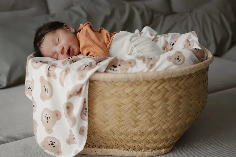 Le nouveau-né dort dans un panier tressé, enveloppé d’une couverture à motifs d’oursons