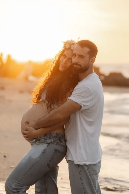 Future maman et son compagnon enlacés au bord de l’eau, dans le soleil couchant