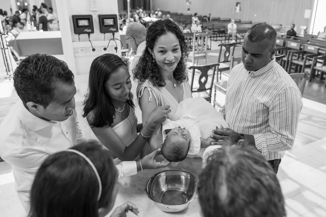 En noir et blanc, parents et proches penchés autour d’un bébé pendant le baptême