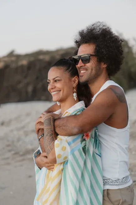 Un couple enlacé en riant sur une plage de sable noir
