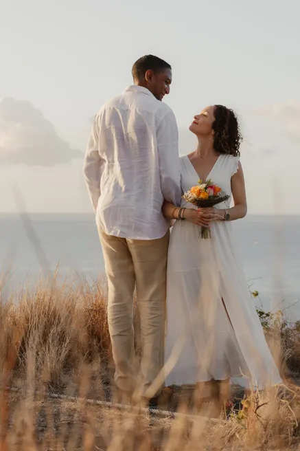 Les mariés se regardent sur une falaise herbeuse face à la mer, bouquet coloré en main