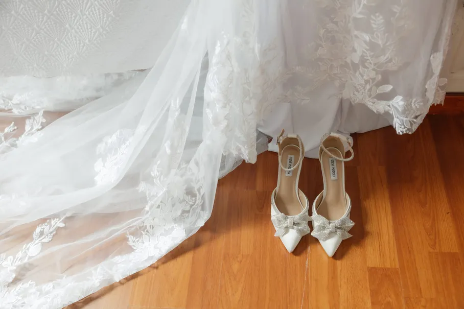 Escarpins à nœud posés sur un parquet, sous la traîne de dentelle de la robe