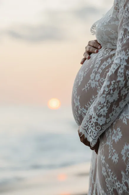 Détail du ventre de la future maman sous la dentelle blanche, soleil bas sur la mer