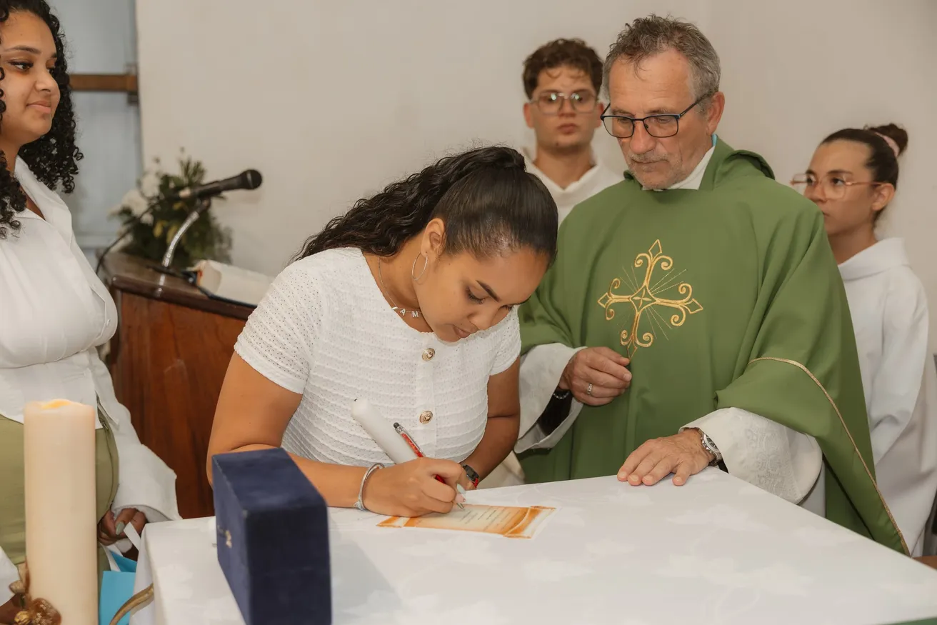 Jeune femme signant le registre sur l’autel, sous le regard du prêtre en chasuble verte