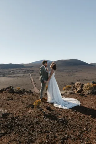 Les mariés se regardent sur un sol de scories, devant les volcans, la traîne étalée derrière elle