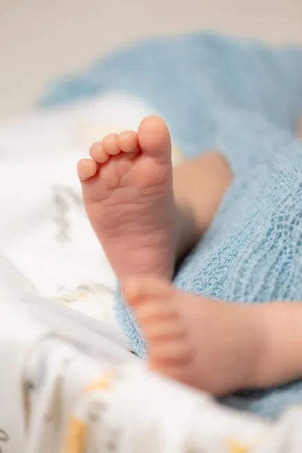 Gros plan sur le petit pied du nouveau-né, les jambes enveloppées d’un lange bleu