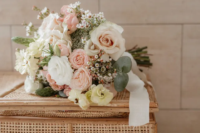 Un bouquet de roses blanches et poudrées posé sur une malle en rotin