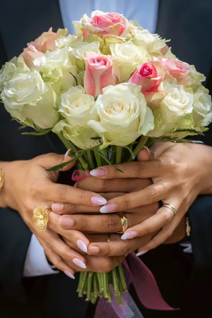 Mains des mariés réunies autour d’un bouquet de roses blanches et roses