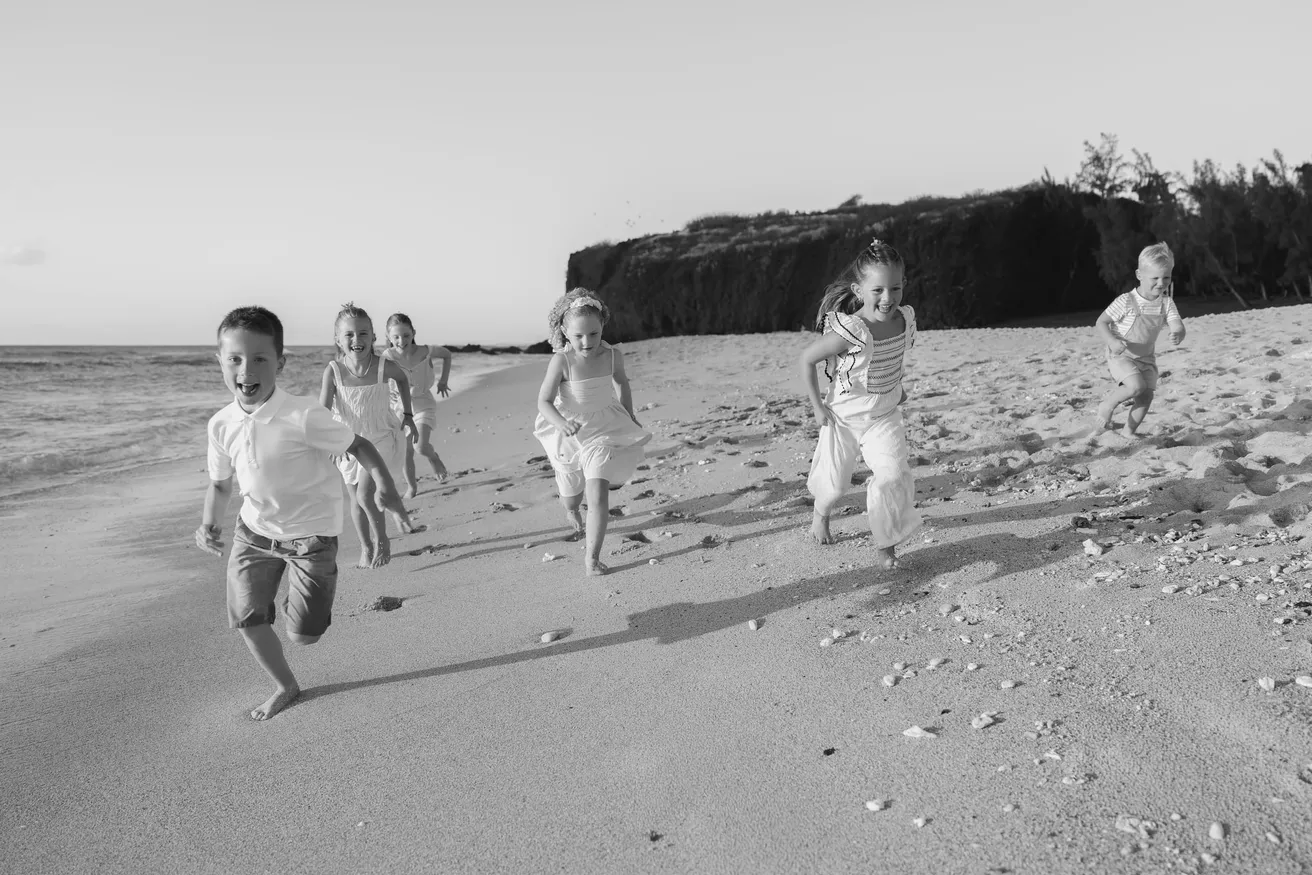 En noir et blanc, des enfants courent sur la plage vers l’objectif