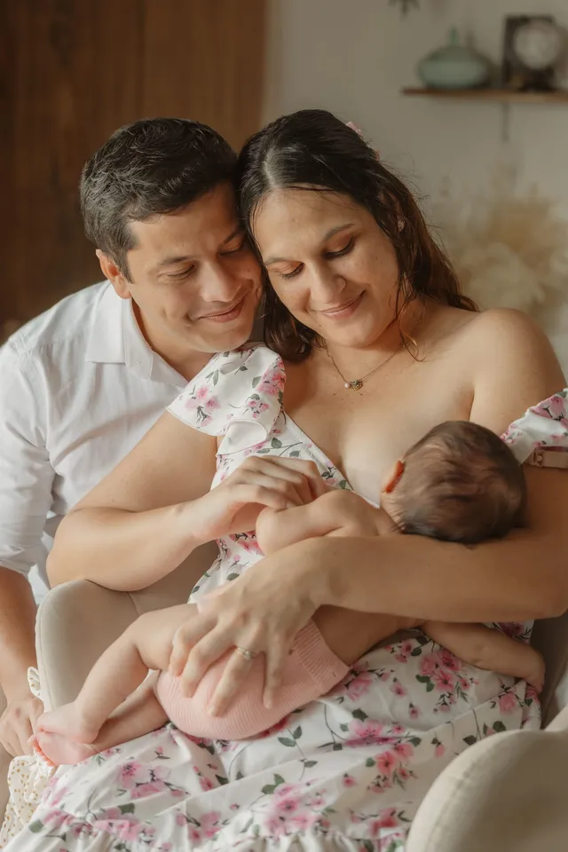 Une maman en robe fleurie berce son bébé, le papa blotti contre elle, dans un fauteuil