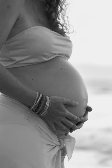 En noir et blanc, détail des mains de la future maman posées sur son ventre drapé