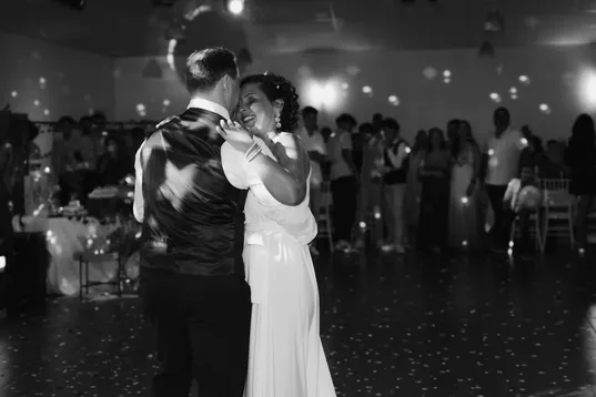 En noir et blanc, les mariés dansent enlacés au milieu de la salle, les invités autour