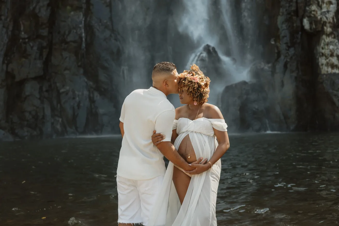Un couple en blanc s’embrasse dans l’eau du bassin, devant une cascade