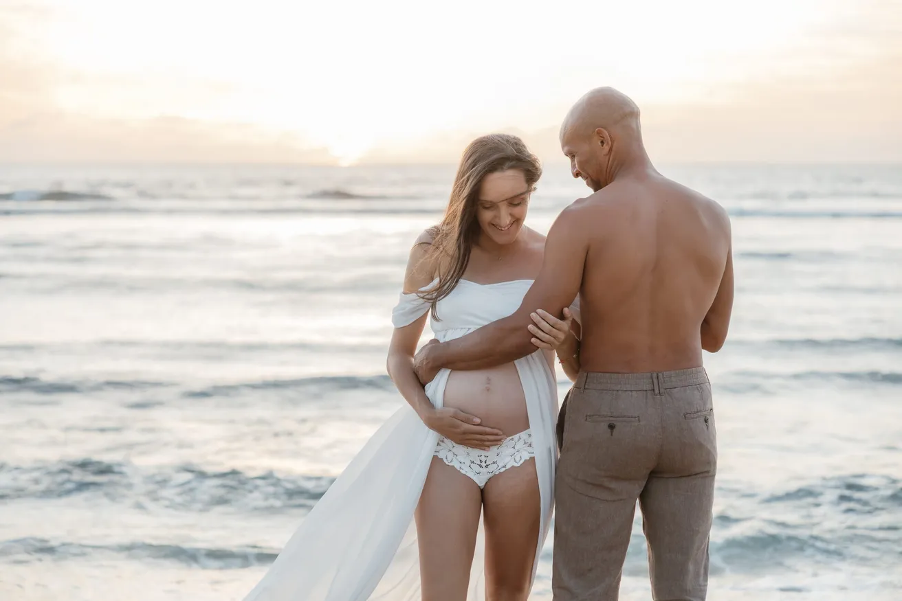Un couple de dos face à la mer, la main de l’homme posée sur le ventre rond
