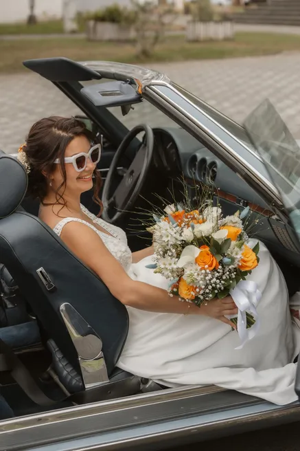 La mariée en lunettes de soleil, son bouquet sur les genoux, assise dans une décapotable