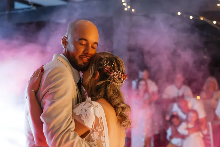 Les mariés dansent enlacés, les yeux fermés, dans la fumée rose de la soirée