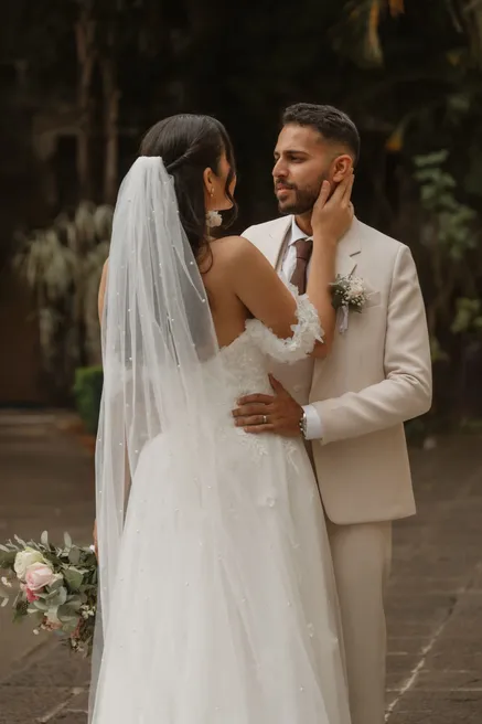 La mariée de dos pose la main sur la joue du marié, qui la regarde en souriant