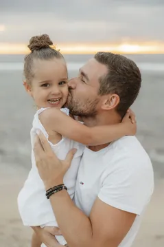 Une petite fille au chignon sourit, enlacée par son père qui l’embrasse sur la joue