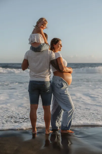 Une famille de dos au bord de l’eau, la fillette sur les épaules du papa