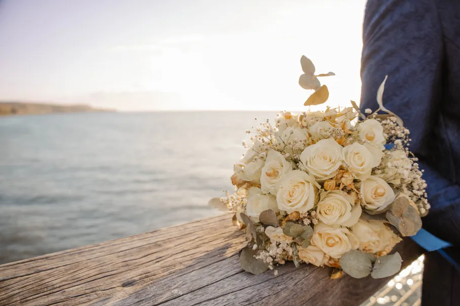Bouquet de roses blanches posé sur une rambarde de bois, face à la mer au soleil couchant