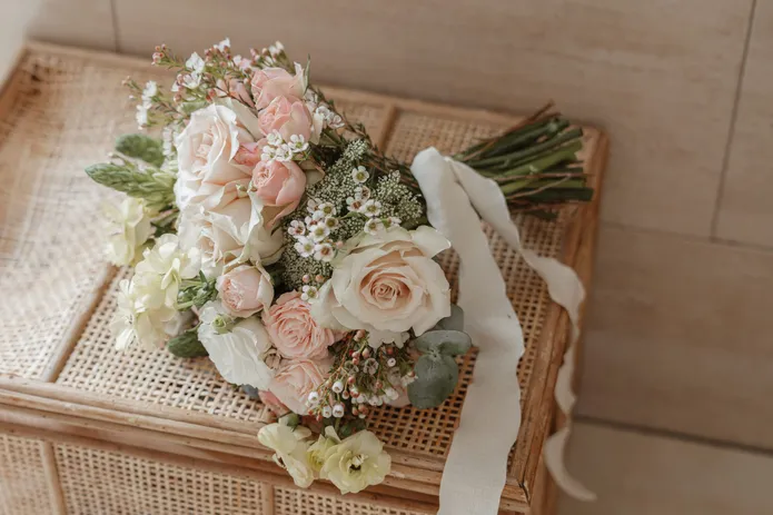Bouquet de roses pâles et de fleurs blanches posé sur un coffret en cannage
