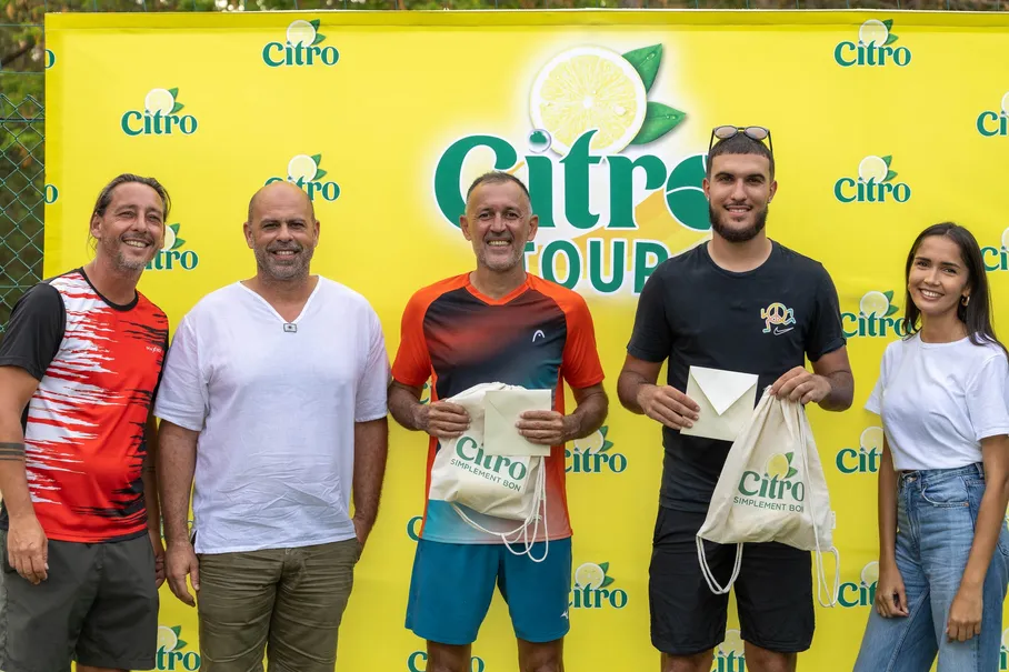 Les joueurs primés d’un tournoi de padel posent devant le panneau jaune de leur sponsor