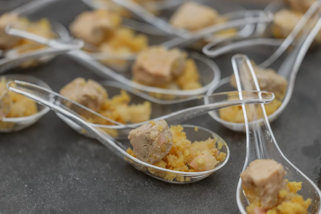 Cuillères apéritives transparentes garnies de bouchées dorées, sur une ardoise