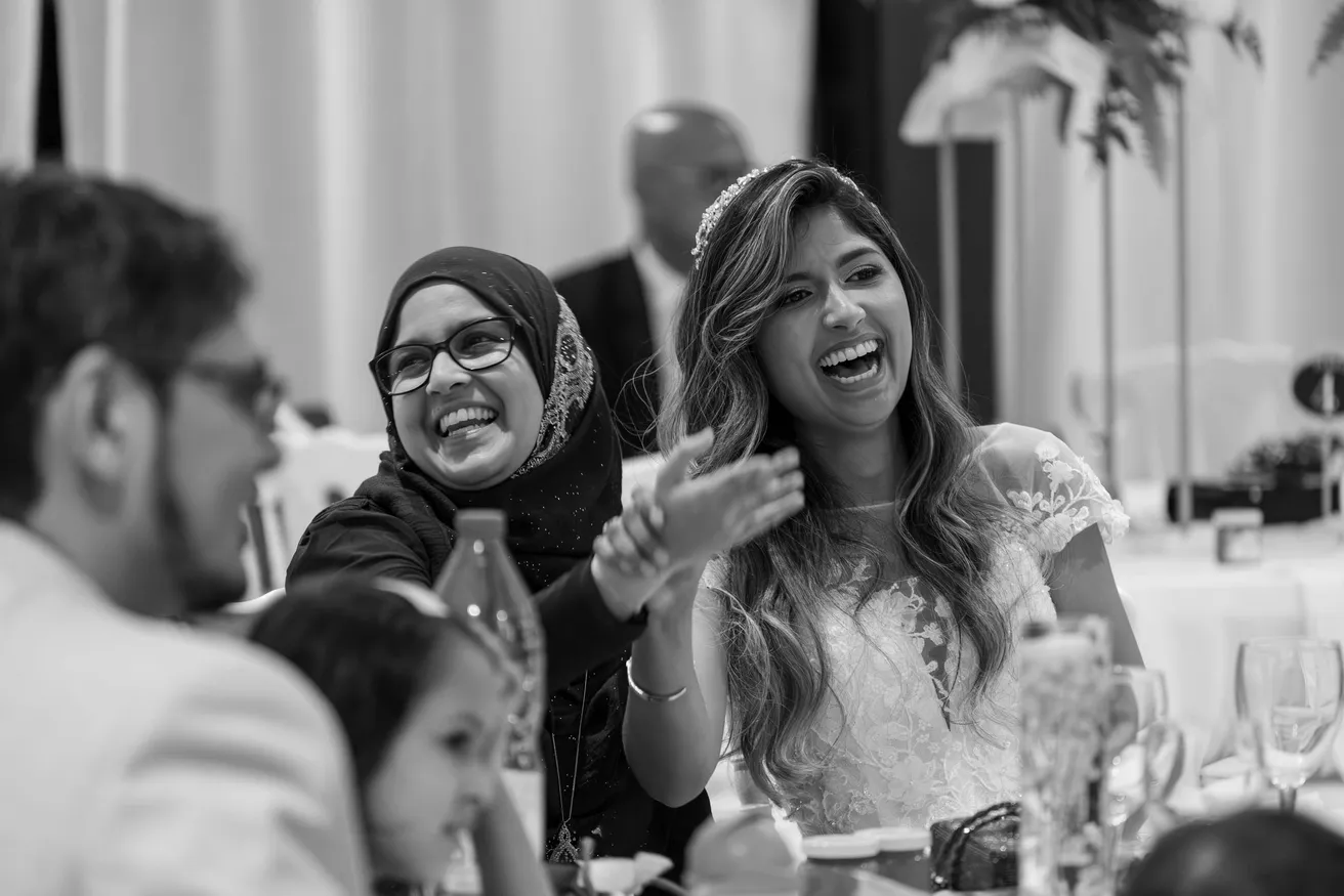 En noir et blanc, la mariée rit aux éclats à table avec une invitée voilée
