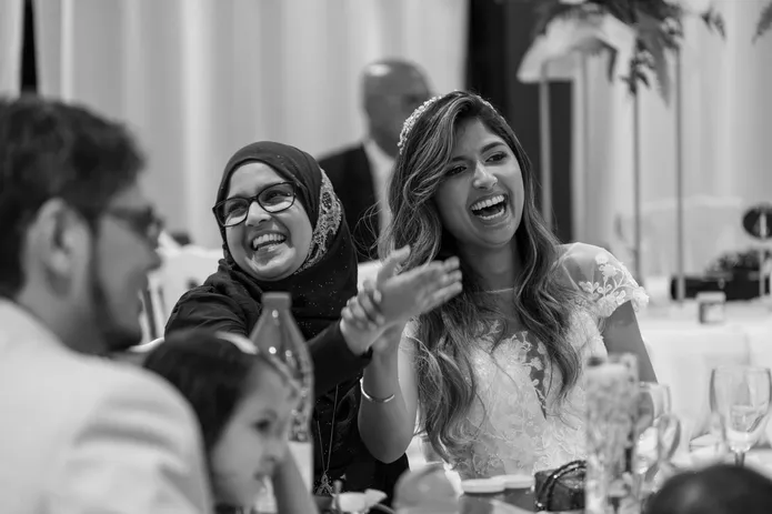 En noir et blanc, la mariée rit aux éclats à table avec une invitée voilée