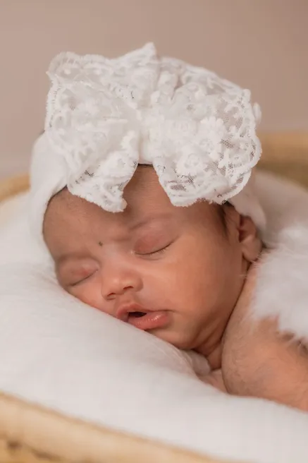 Le nouveau-né dort la bouche entrouverte, coiffé d’un turban de dentelle blanche