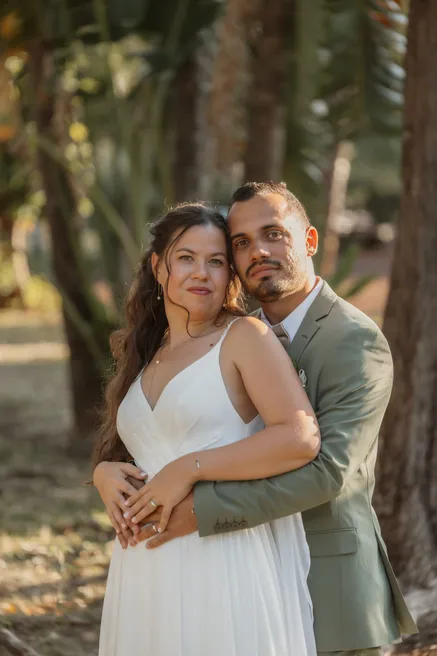 Le marié enlace la mariée par derrière, dans la lumière dorée d’un sous-bois
