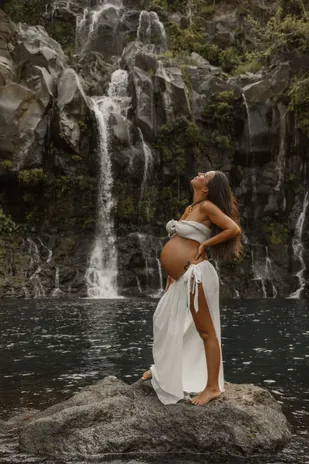 Future maman debout sur un rocher, main sur la hanche, cascades en arrière-plan