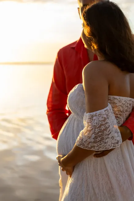 Détail de la future maman en dentelle blanche contre son compagnon en chemise rouge, reflets dorés