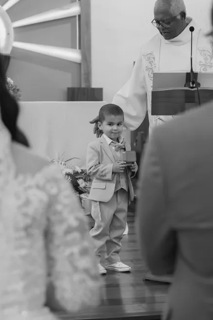 En noir et blanc, un petit garçon en costume s’avance dans l’église devant le prêtre