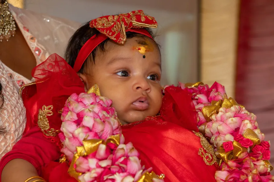 Gros plan sur le bébé en robe rouge, nœud dans les cheveux et guirlandes de fleurs roses