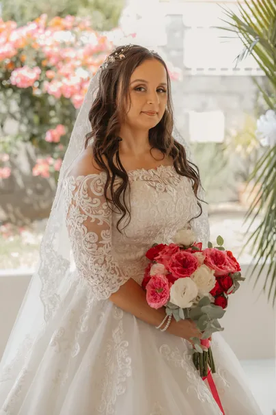 La mariée en robe de dentelle aux épaules dénudées, bouquet rouge et blanc à la main