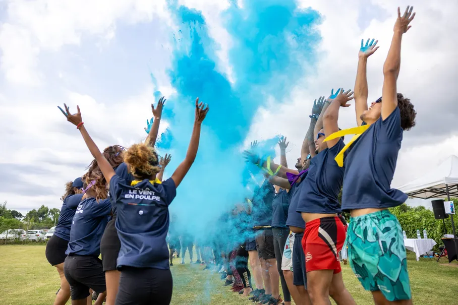 Des équipes en tee-shirts bleus lancent de la poudre colorée en l’air, sur une pelouse