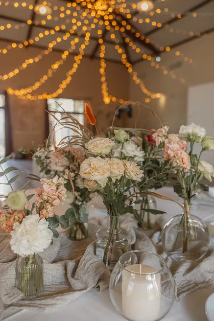 Table de réception fleurie de bouquets pastel, sous des guirlandes lumineuses