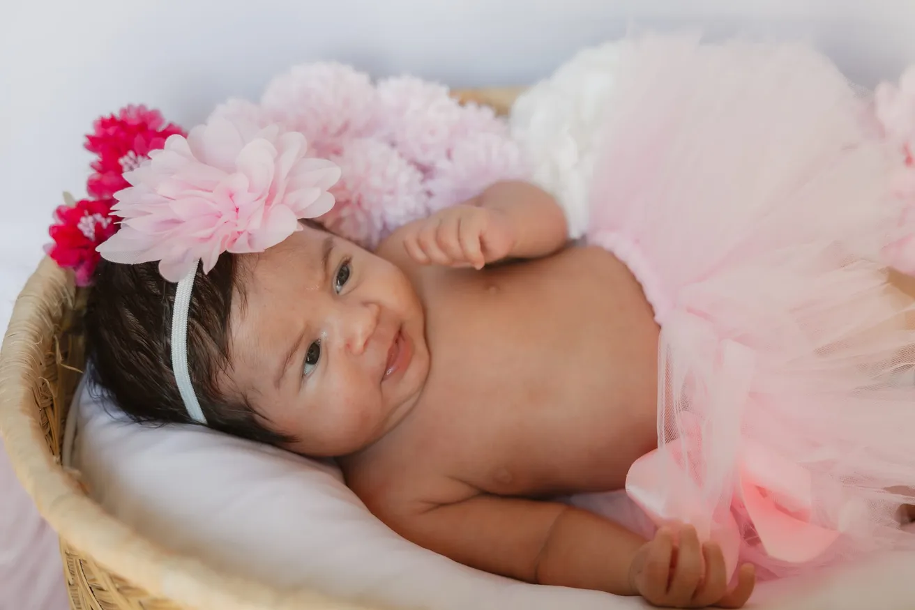 Le nouveau-né sourit dans un panier, avec un bandeau à fleur rose et un tutu rose
