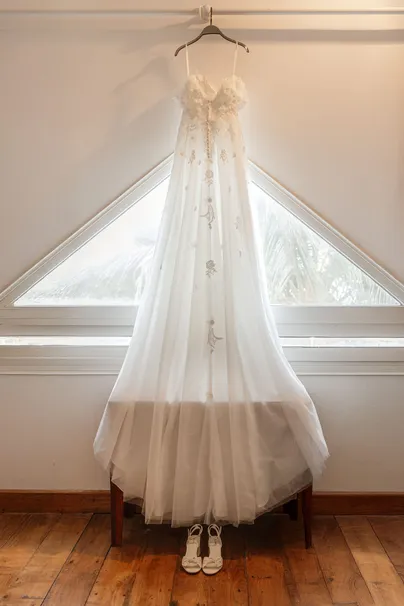 Robe de mariée en tulle suspendue devant une fenêtre triangulaire, escarpins posés dessous