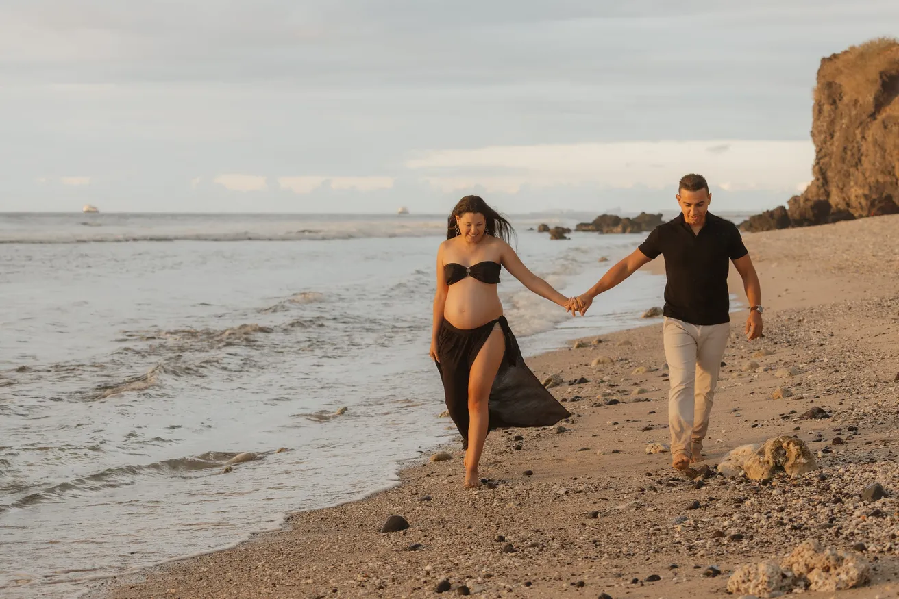 Un couple qui marche main dans la main au bord de l’eau, au pied d’une falaise