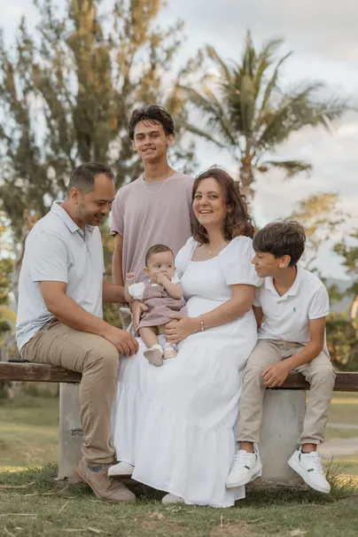 Une famille de cinq réunie sur un banc sous les arbres, la mère tient le bébé sur ses genoux