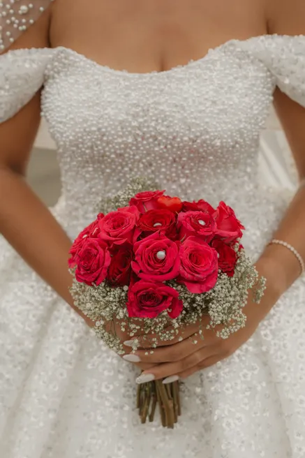 Gros plan sur un bouquet de roses rouges tenu devant une robe perlée