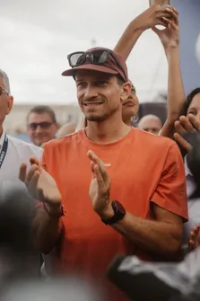 Un spectateur en casquette et tee-shirt orange applaudit, souriant, au milieu de la foule