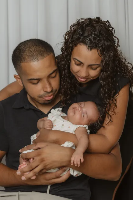 Les deux parents tiennent leur nouveau-née contre eux, sur fond sombre