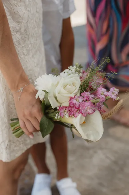 Main tenant un bouquet de roses blanches et de fleurs roses contre une robe de dentelle