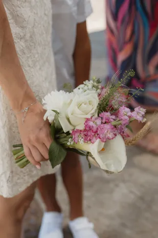 Main tenant un bouquet de roses blanches et de fleurs roses contre une robe de dentelle